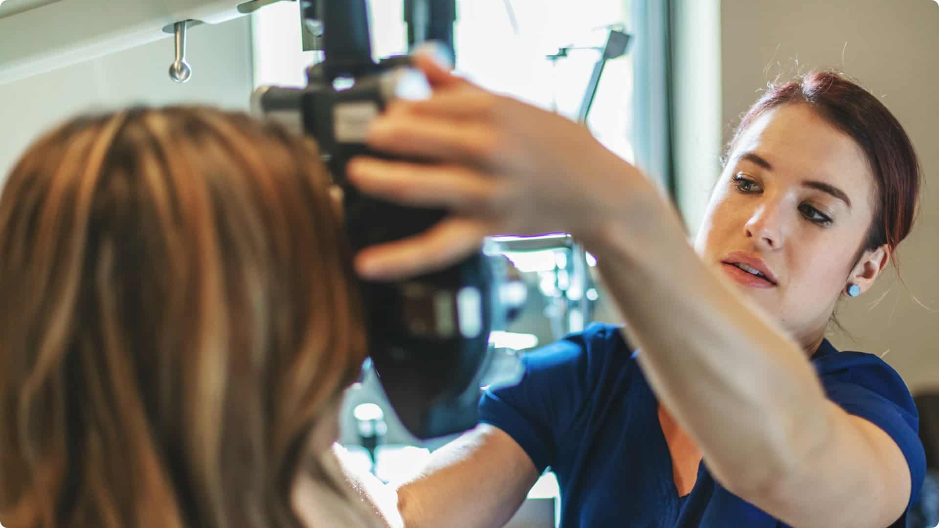 Image of a female nurse helping a patient get into position to have her eyes scanned